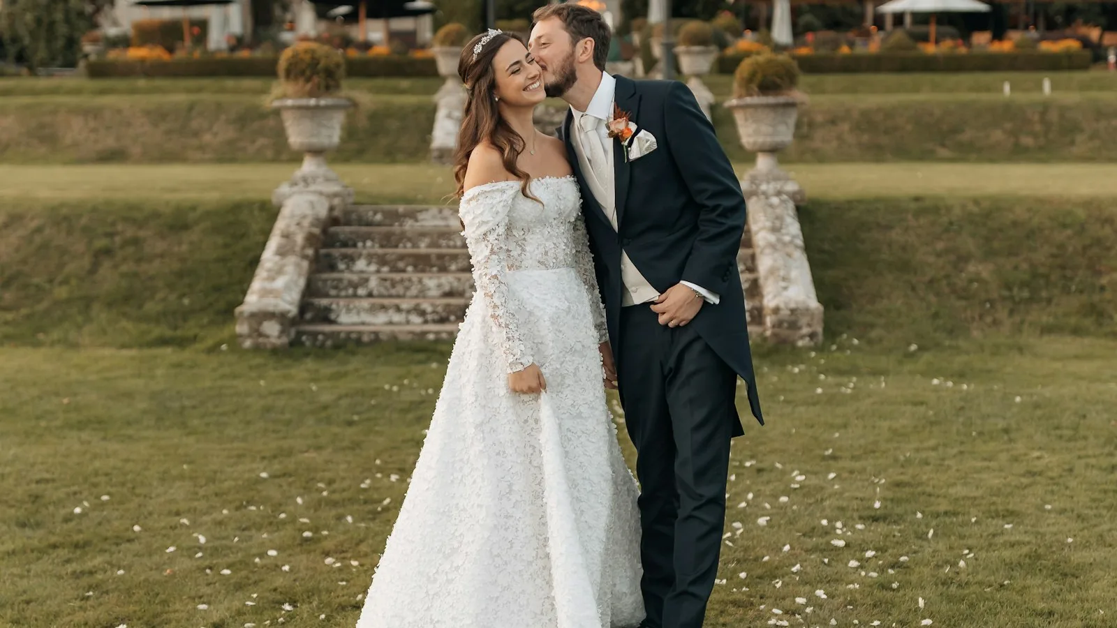 Yeşil bir bahçede merdivenlerin yanında duran ve birbirine gülümseyen bir çift