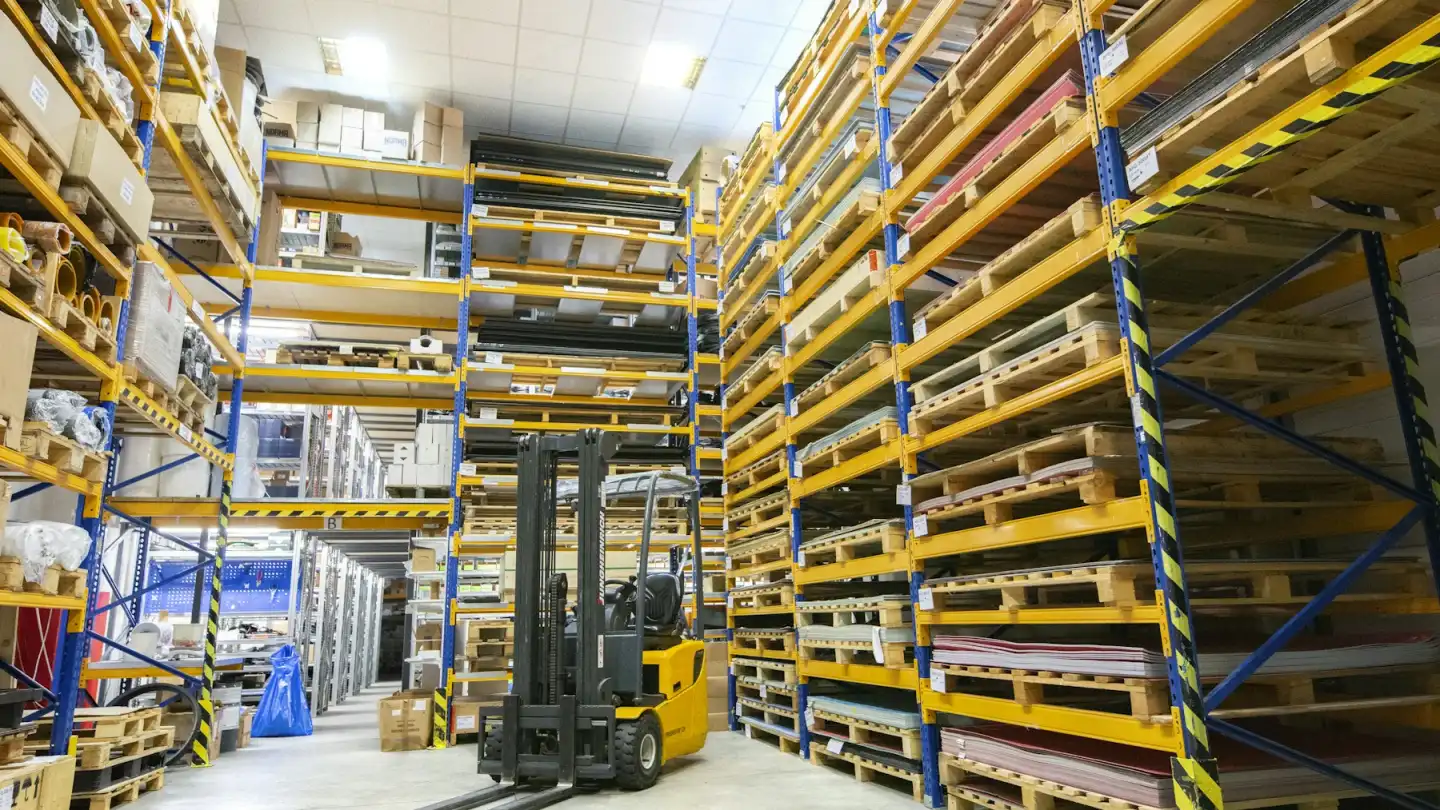 Sarı raflar ve forkliftlerin dizili olduğu büyük depo koridoru
